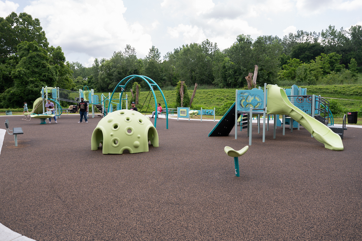 An outdoor playground featuring spinning elements, slides, swings, platforms, rope webs, climbing walls, musical instruments, and more.