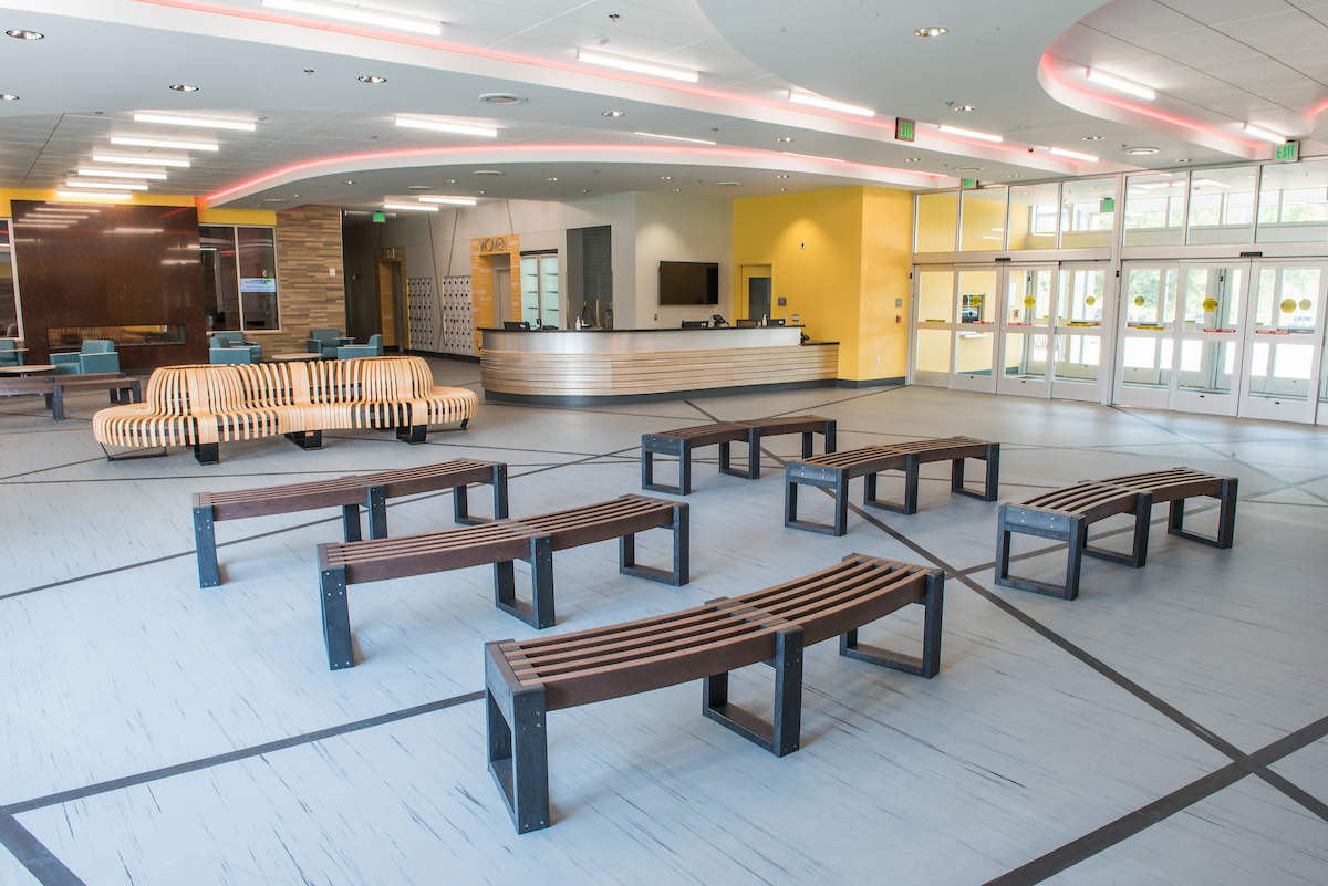 A large lobby space with a curved reception desk next to a set of multiple entrance doors, and about ten curved wooden benches spread out in the lobby. In the rear of the lobby are restrooms and a lounge with a fireplace.