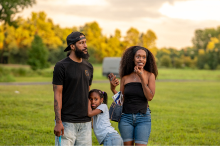 Two adults and a child stand together on a grassy field, watching an outdoor event.