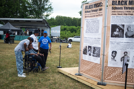 Visitors view an educational exhibit about Black music history at an outdoor festival.