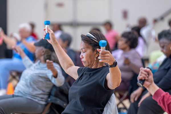 Seniors work out with small hand weights while sitting in folding chairs.