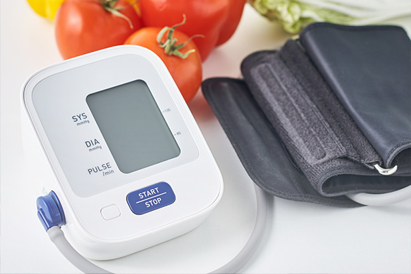 A digital blood pressure cuff next to fresh produce, including lettuce and tomatoes.