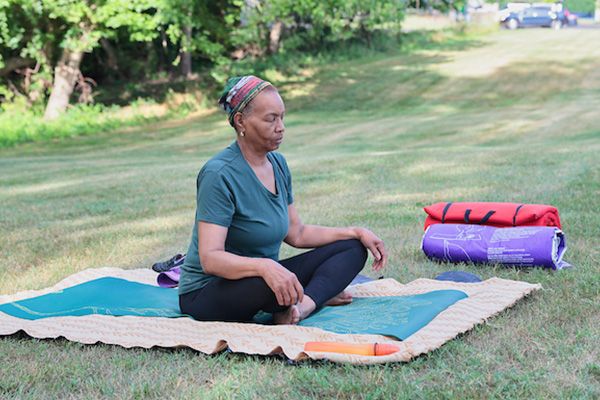 A woman calmly meditating on a yoga mat in a grass field.