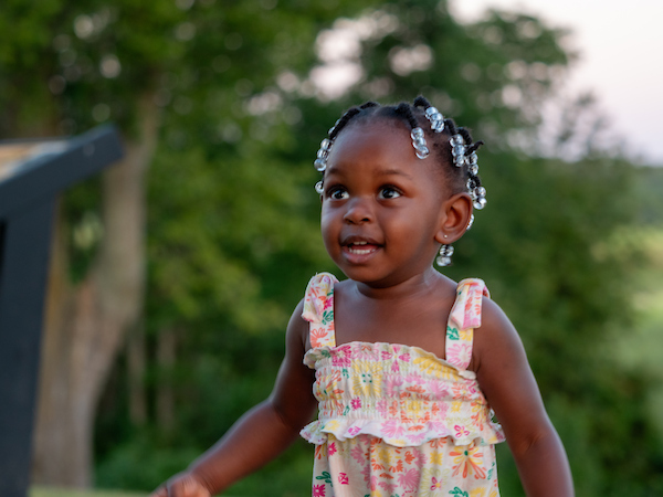 A small child outside near a wooded area.