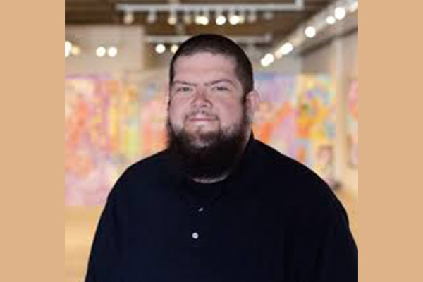 A man in a black shirt with a blurry art gallery behind him.