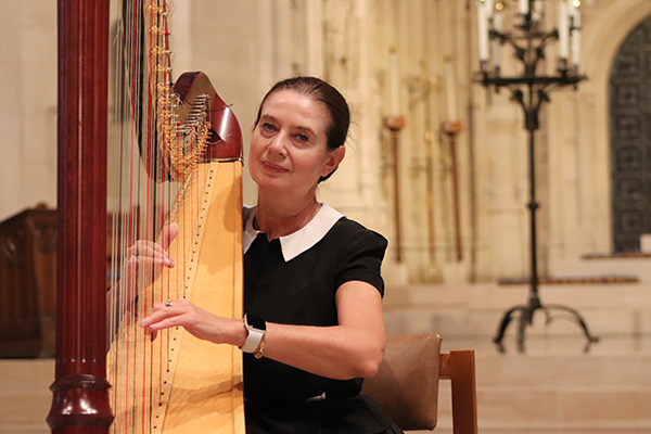 A seated woman plays a harp in a stone church or cathedral hall.