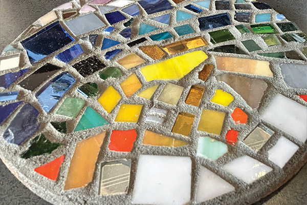 A round, concrete coaster with a colorful glass mosaic on the top.