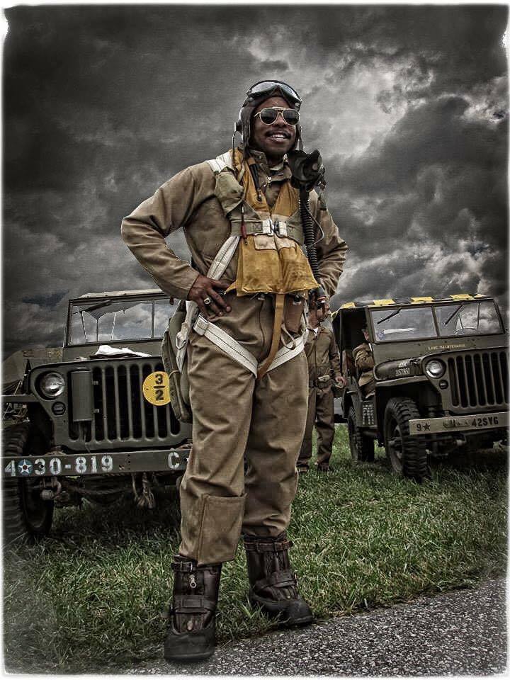 Person in vintage military flight gear stands between two military jeeps outdoors beneath dramatic storm clouds.