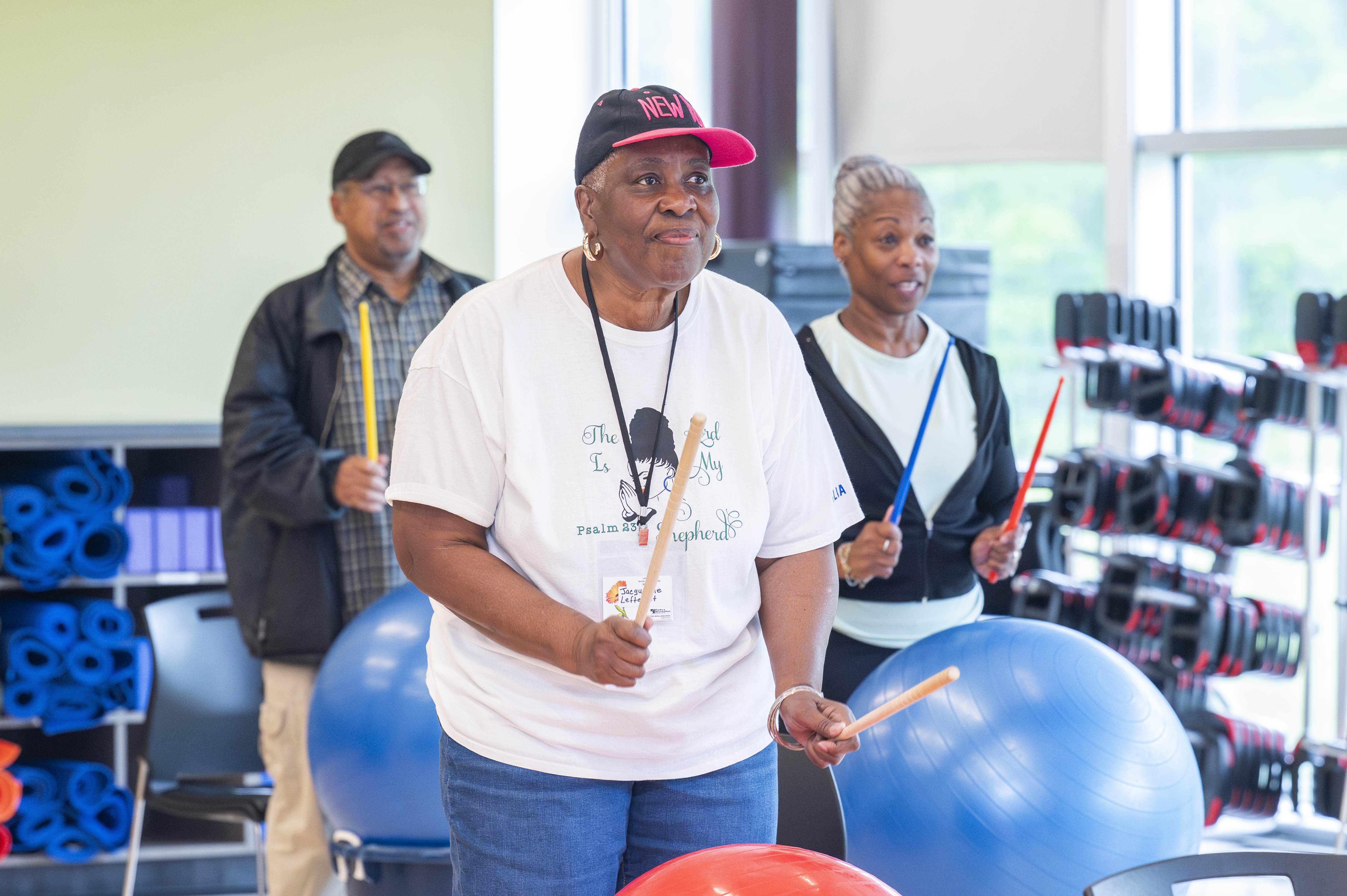 Older adults holding drumsticks and playing drum fitness on large blue and red stability balls during a workout class.